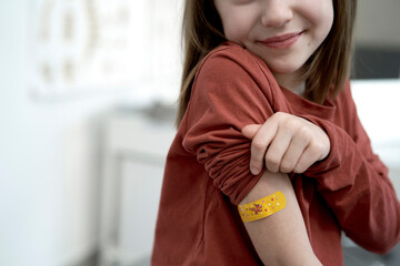 Smiling girl showing adhesive bandage after vaccination in clinic