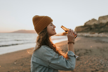 Smiling woman with beer bottle standing at beach