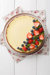 Delicate sweet New York cheesecake decorated with fresh berries and mint close-up on a plate on the table. Vertical top view from above
