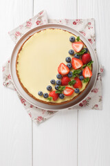 Classic Freshly New York Cheesecake with fresh berries and mint closeup on the plate on the wooden table. Vertical top view from above