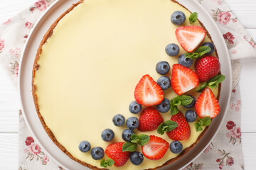 Whole round new york cheesecake with strawberries, blueberries and mint close-up on a plate on the table. Horizontal top view from above
