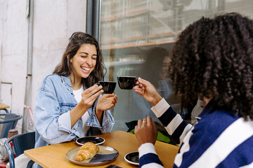 Cheerful young friends toasting coffee cup and enjoying at sidewalk cafe