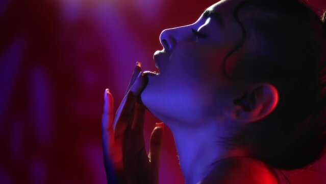Sensual woman touching lips neck finger shadow silhouette dark neon studio background closeup