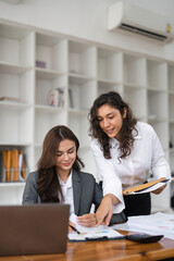 Two diverse female smiling while working together at a boardroom table during a meeting in a modern office