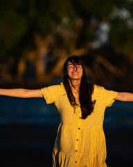 girl wearing yellow dress admires colourful sunset wading in the shallow water at nudgee beach,...