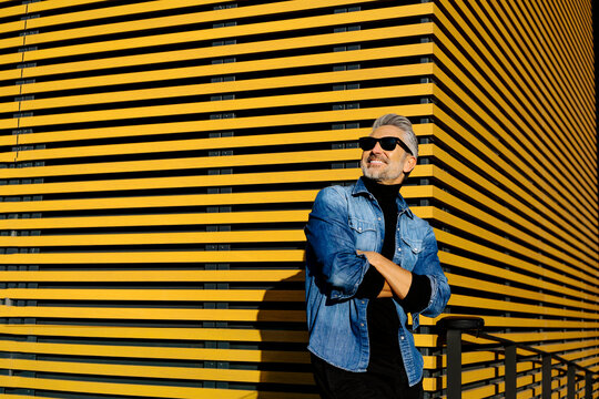 Mature man standing with arms crossed in front of yellow striped building