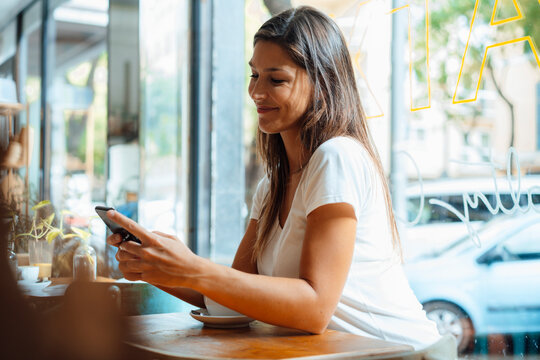 Smiling woman text messaging through smart phone in cafe