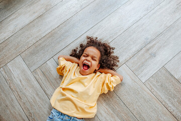 Cute girl yawning and lying on wooden floor at home