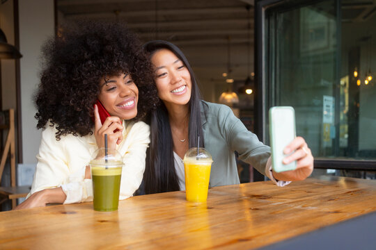 Young woman taking selfie with friend talking on smart phone at cafe