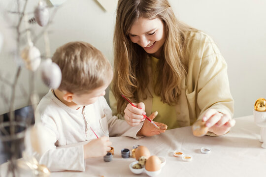 Happy mother and son decorating Easter eggs at home