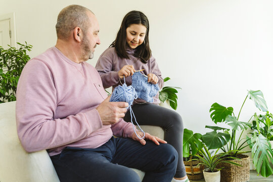 Smiling senior man assisting granddaughter in knitting sweater at home