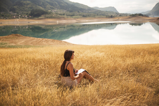 Young woman with sketch pad sitting in front of Rama Lake