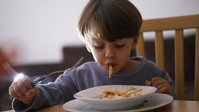 Male kid eating pasta spaghetti by himself. Child spinning pasta with hands and fork. One small boy eats Italian food for dinner