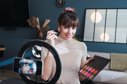 Smiling woman filming make-up vlog holding palette at home