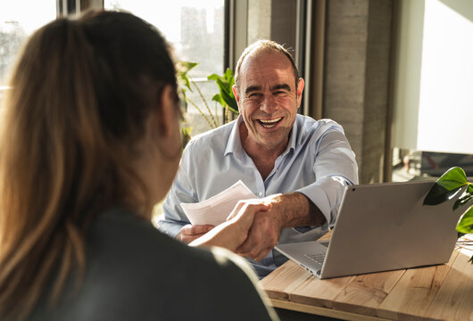 Happy mature businessman doing handshake with colleague in office