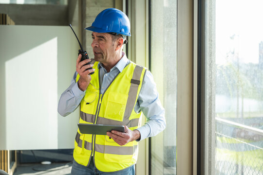 Engineer using walkie talkie holding tablet PC in office