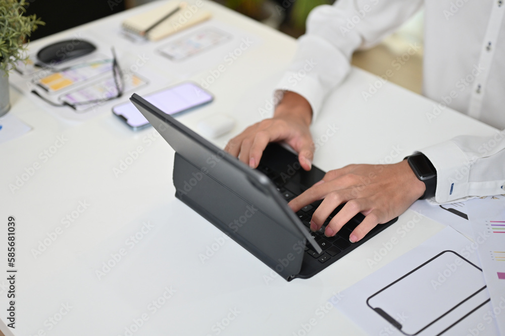 Poster cropped shot of ux designer typing on wireless keyboard of digital tablet, working on project at off