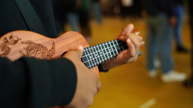 Boy in a black sweater plays single simple chords on a wooden ukulele close-up