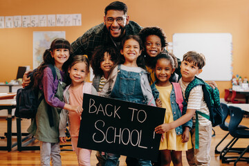 Teacher and his primary school class holding a back to school sign, excited to start a new year