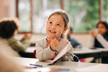 Excited little girl learns to draw with a colour pencil in an art class - obrazy, fototapety, plakaty