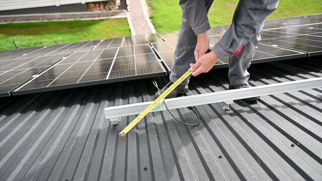 Close up view of competent technician making measurements for exact calculations. Adjusting PV solar panel on a roof. Engineer in helmet making calculations of solar cell with a measuring tape.