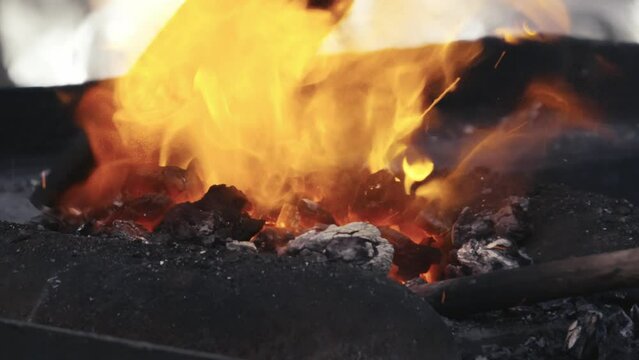 A blacksmith scoops hot coals onto a molten metal rod. Slow motion close up shot.
