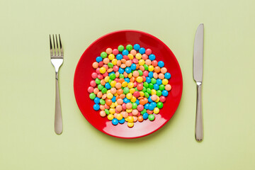 cutlery on table and sweet plate of candy. Health and obesity concept, top view on colored background
