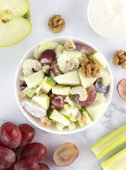 Bowl of waldorf salad with apple, celery, grapes, walnuts and yogurt on a white background. Top view. 
