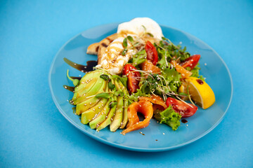 Healthy breakfast. Avocado and salmon, poached egg and toast, salad and vegetables. Microgreens on a plate. Food bowl. Lunch on a blue plate. Sauce and sesame seeds, lemon tomatoes. Top view.