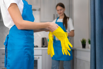 Close-up of the hands of a professional cleaning lady from a cleaning company wearing yellow gloves against the background of a second employee before cleaning. Personal protective equipment