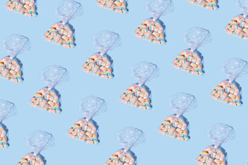 Pattern made of marshmallow candies in wrapped transparent plastic bag on pastel blue background....