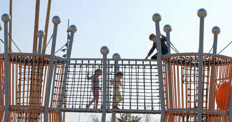 Toddler girls and boy in the park climbing on a rope structure