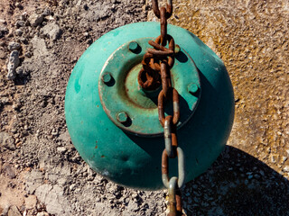 blue buoy with rusty chain on asphalt