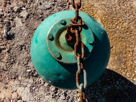blue buoy with rusty chain on asphalt