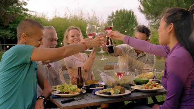 Happy middle age friends toasting with wine during barbecue garden dinner party in the evening. 4k video. 