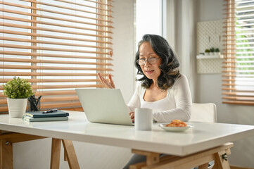 Professional 60s Asian-aged businesswoman having an online meeting with her team