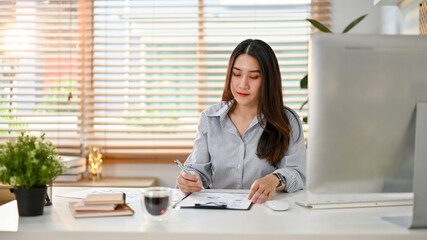 Focused young Asian businesswoman examining business financial data report at her desk