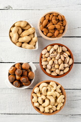 Nuts: almonds, pistachios, peanuts, hazelnuts and cashews in bowls on white wooden background with copyspace