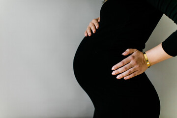 Babybauch und Hände einer Schwangeren Frau im engen schwarzen Kleid