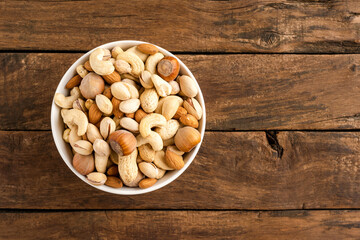 Nuts: almonds, pistachios, peanuts, hazelnuts and cashews in bowl on wooden background with copyspace