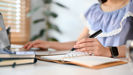 Cropped image of an Asian woman writing something on her notepad while using laptop