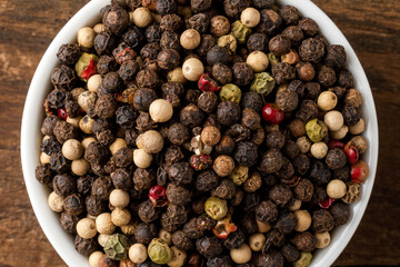 Mixed peppercorns in bowl on rustic wooden table. Top view