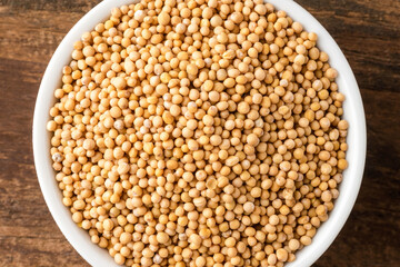 White mustard seeds in bowl on rustic wooden table. Top view