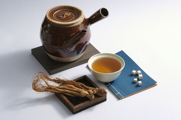 A wooden tray of Angelica root displayed with a bowl of medicine, an earthen pot and few Poria...
