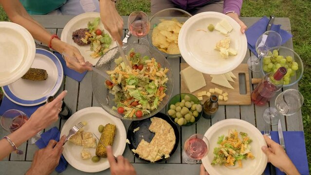 Top view 4k video of unrecognizable people passing plates and serving food during outdoors garden dinner party.
