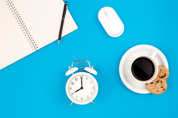 Alarm clock and coffee on blue background, work concept, flat lay.