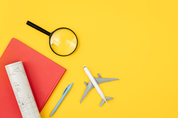 Airplane model, notebook, map and magnifier on yellow background, flat lay.