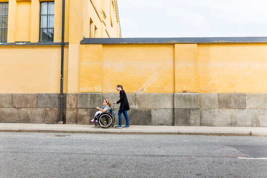 Assistant helping disabled woman in wheelchair move around city