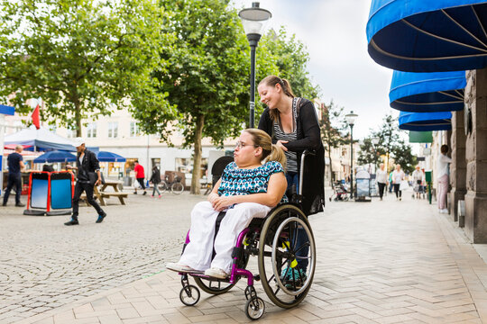 Assistant helping disabled woman in wheelchair move around city