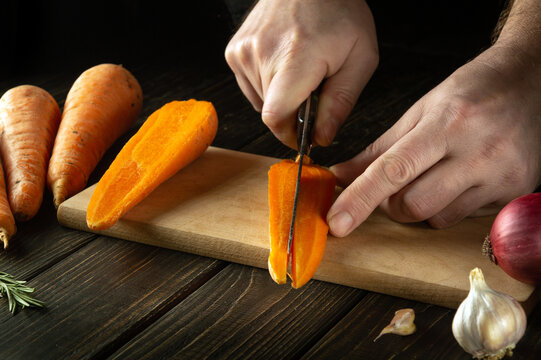 The Chef Cuts Fresh Carrots On A Wooden Cutting Board. Close-up Of Cook Hands While Preparing Vegetarian Food With Vegetables